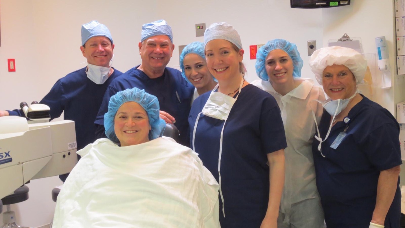 Six members of the Rand team gathered around a patient in the laser suite, all smiling for the camera.
