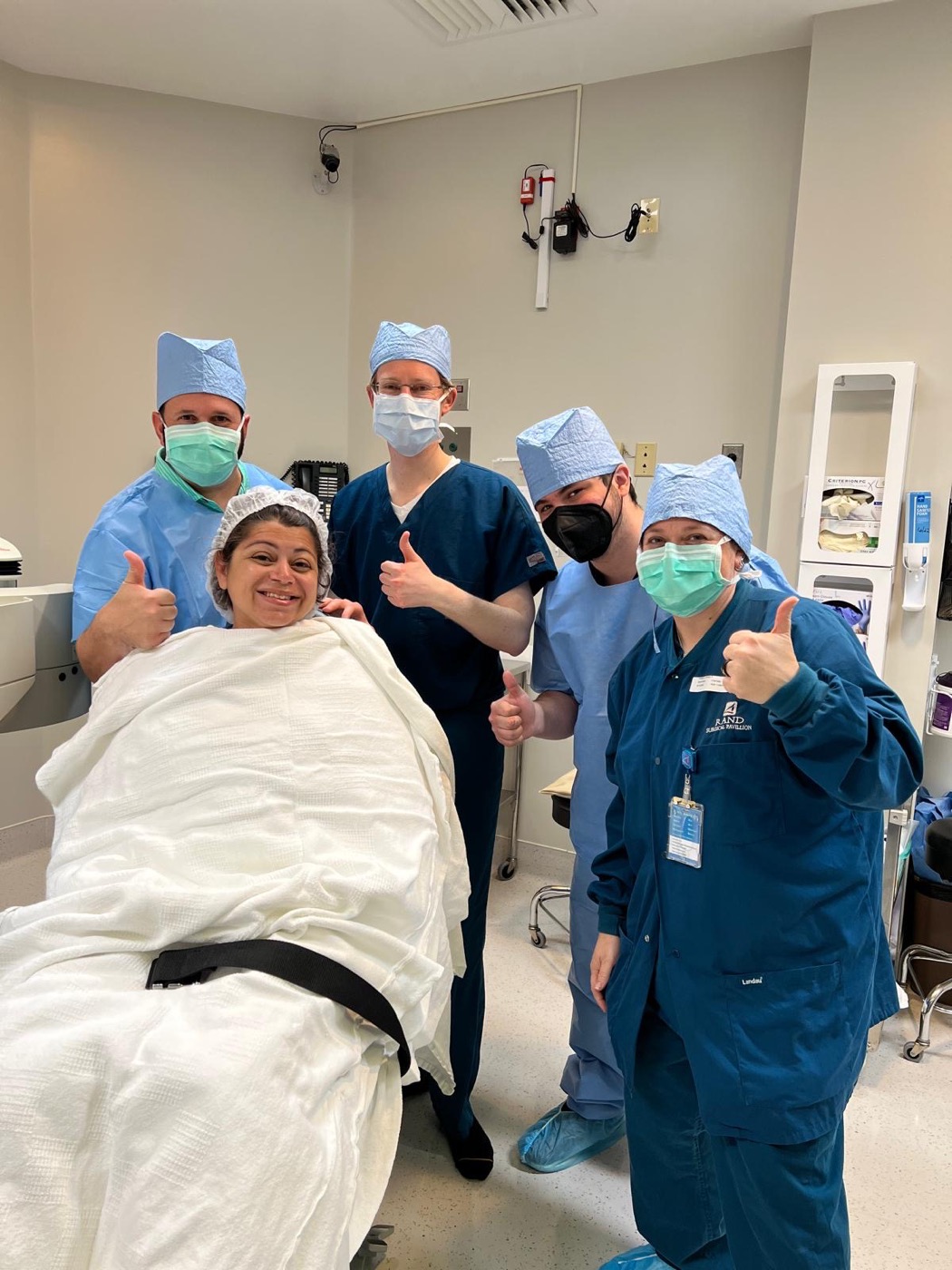 Four members of the surgical team standing with a patient after her procedure, everyone giving a thumbs up.